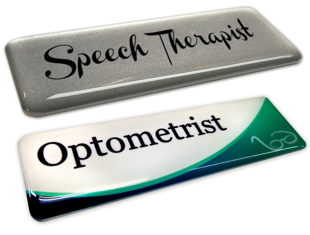 A aluminium silver Speech Therapist name badge and a standard Optometrist name badge
